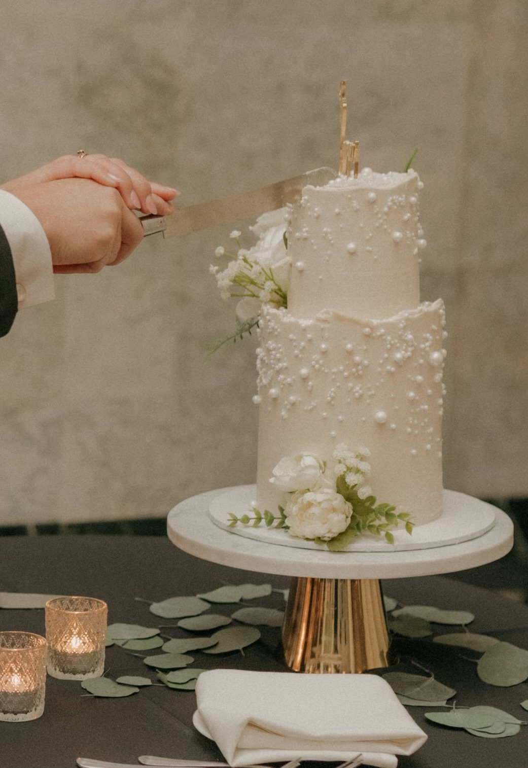 Two-tier white pearl-detailed wedding cake being cut