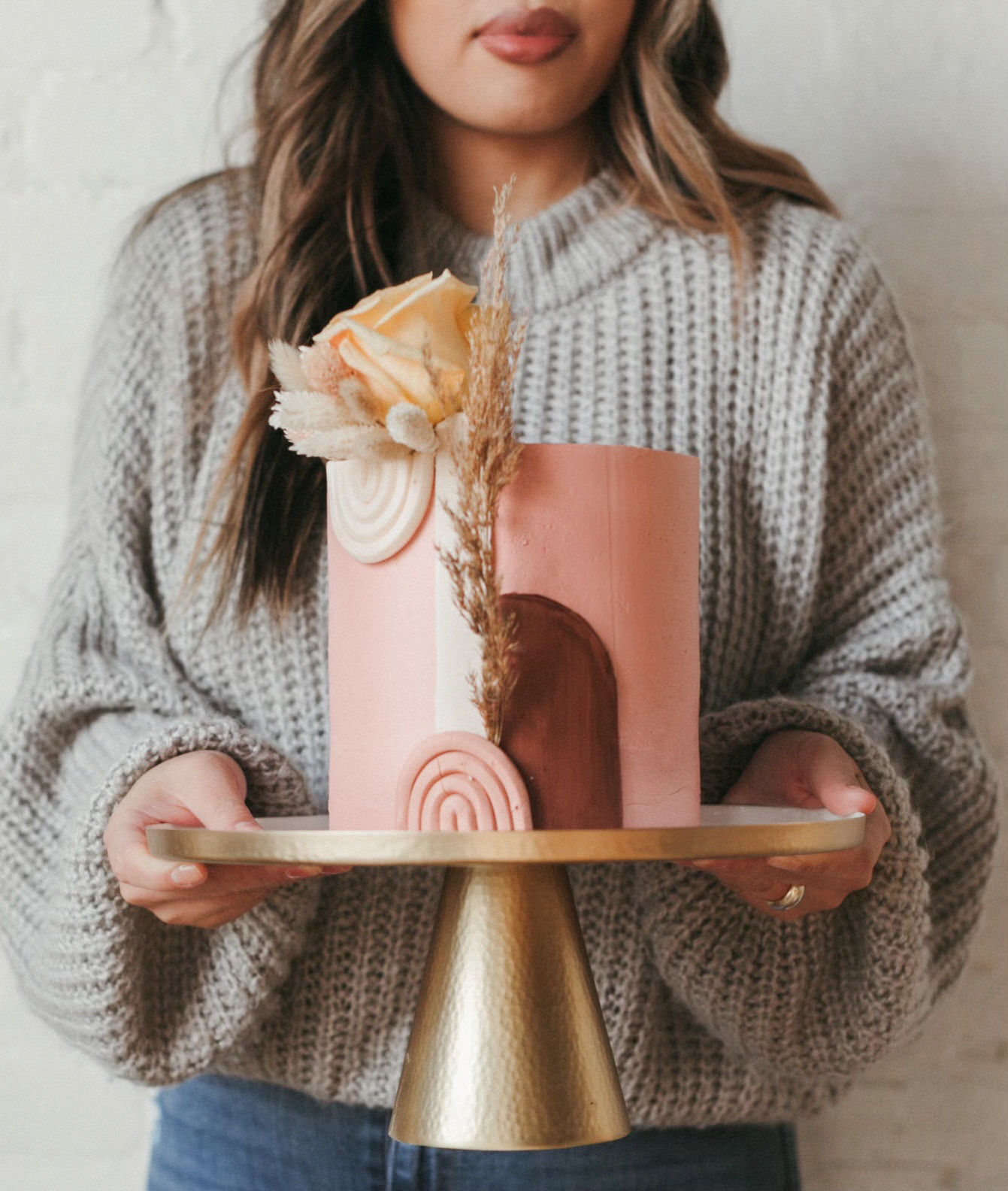 Vickie holding a pink buttercream cake with arch details, pampas, and a dried rose