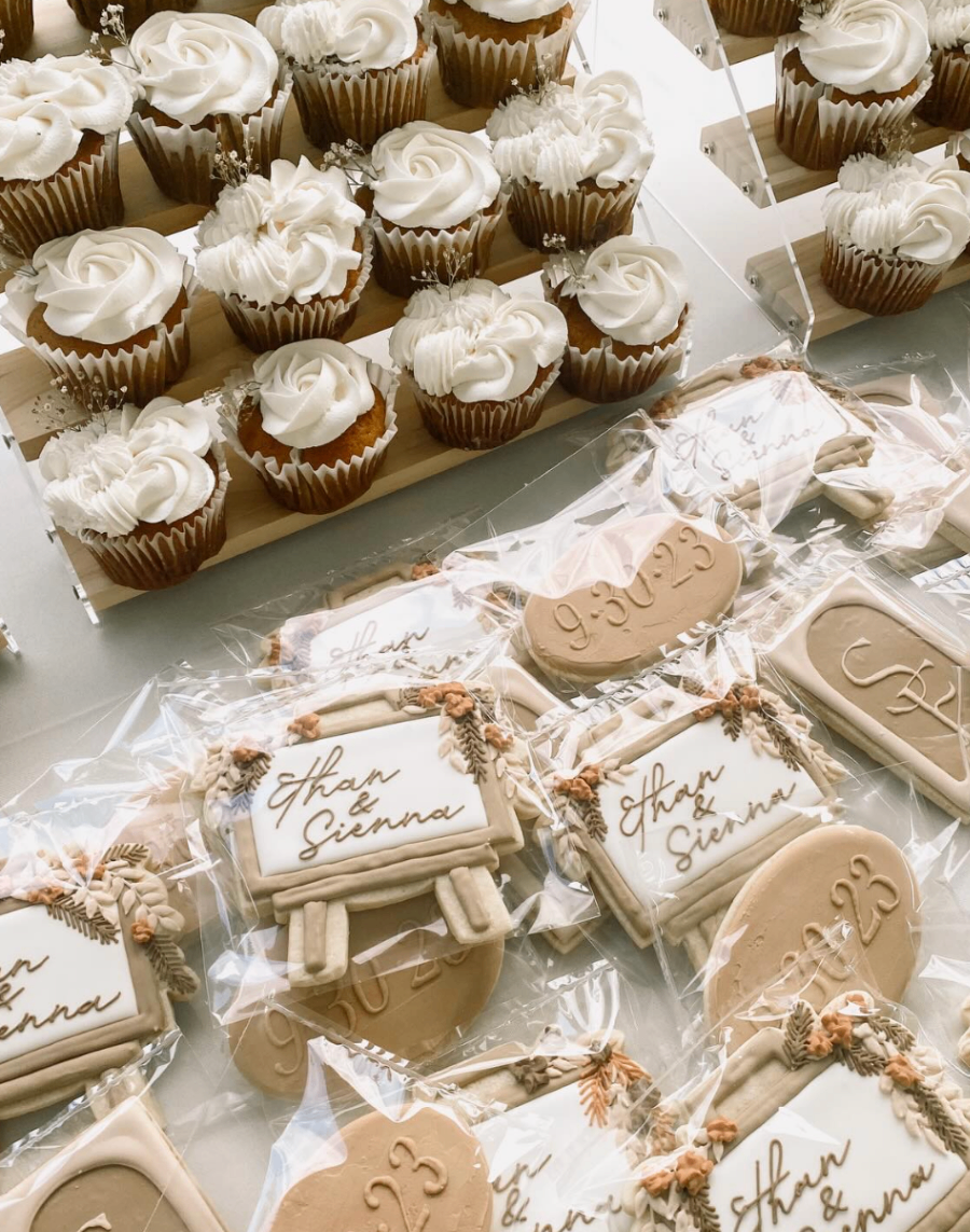 Vanilla cupcakes with tall white swirls beside individually wrapped celebration cookies